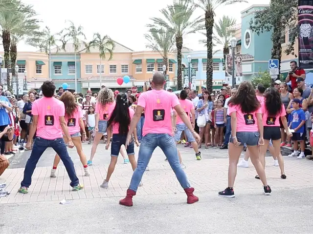 A group of dancers wearing matching pink t-shirts performing a synchronized outdoor flash mob dance routine in Miami by StepFlix Entertainment.