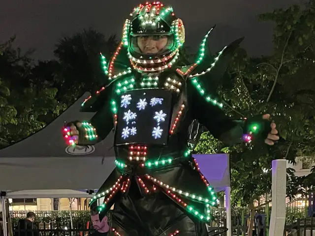 An LED robot dancer on stilts wearing a glowing light-up suit and helmet at a night event in Miami by StepFlix Entertainment.