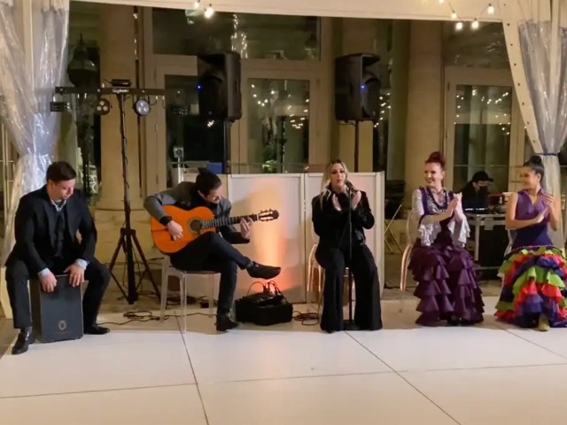 Flamenco ensemble with guitarist, cajón player and dancers in traditional dresses at a ballroom event.