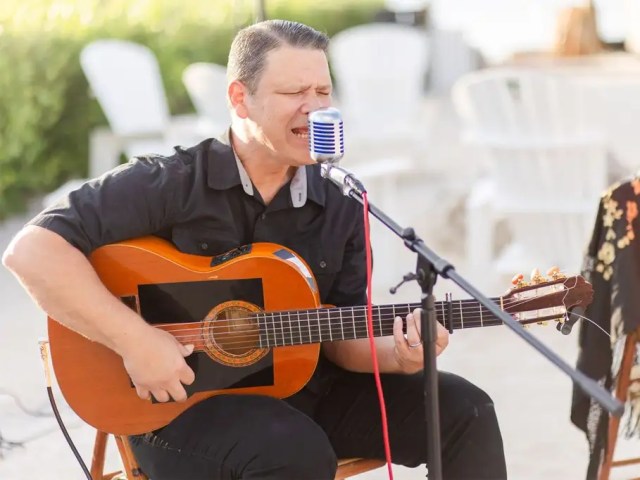 panish guitarist performing a live acoustic set into a microphone at an outdoor event.