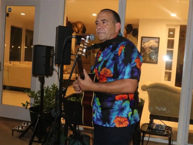 Flamenco guitarist performing while a singer in a floral dress claps palmas at an indoor event.